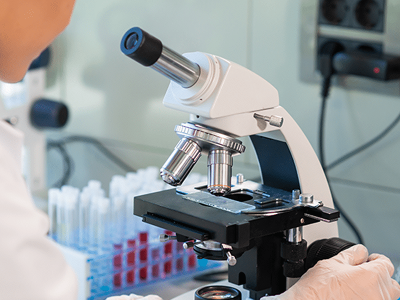 Scientist examining a sample under a microscope to analyze drug compounds.