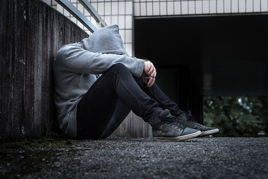 Young person sitting alone, overwhelmed by the effects of addiction.