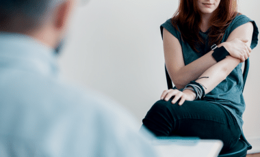 Woman sitting with arms crossed during a therapy session, reflecting on addiction