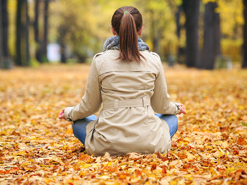 A person meditating outdoors among fallen leaves, practicing mindfulness as a natural remedy.
