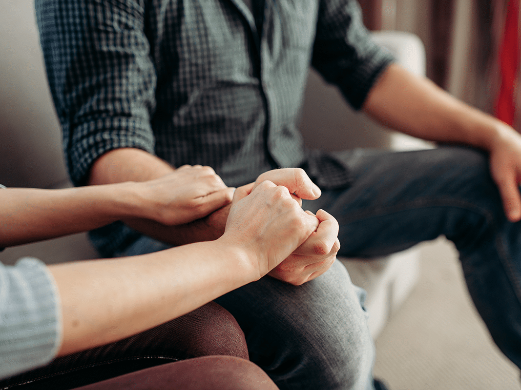 Family members sitting on couch holding hands in support of dual diagnosis recovery